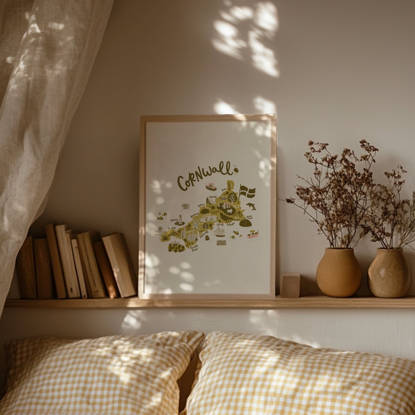 Lifestyle shot of illustrated Cornwall map print. Framed print on a shelf above a bed with gingham bedding.