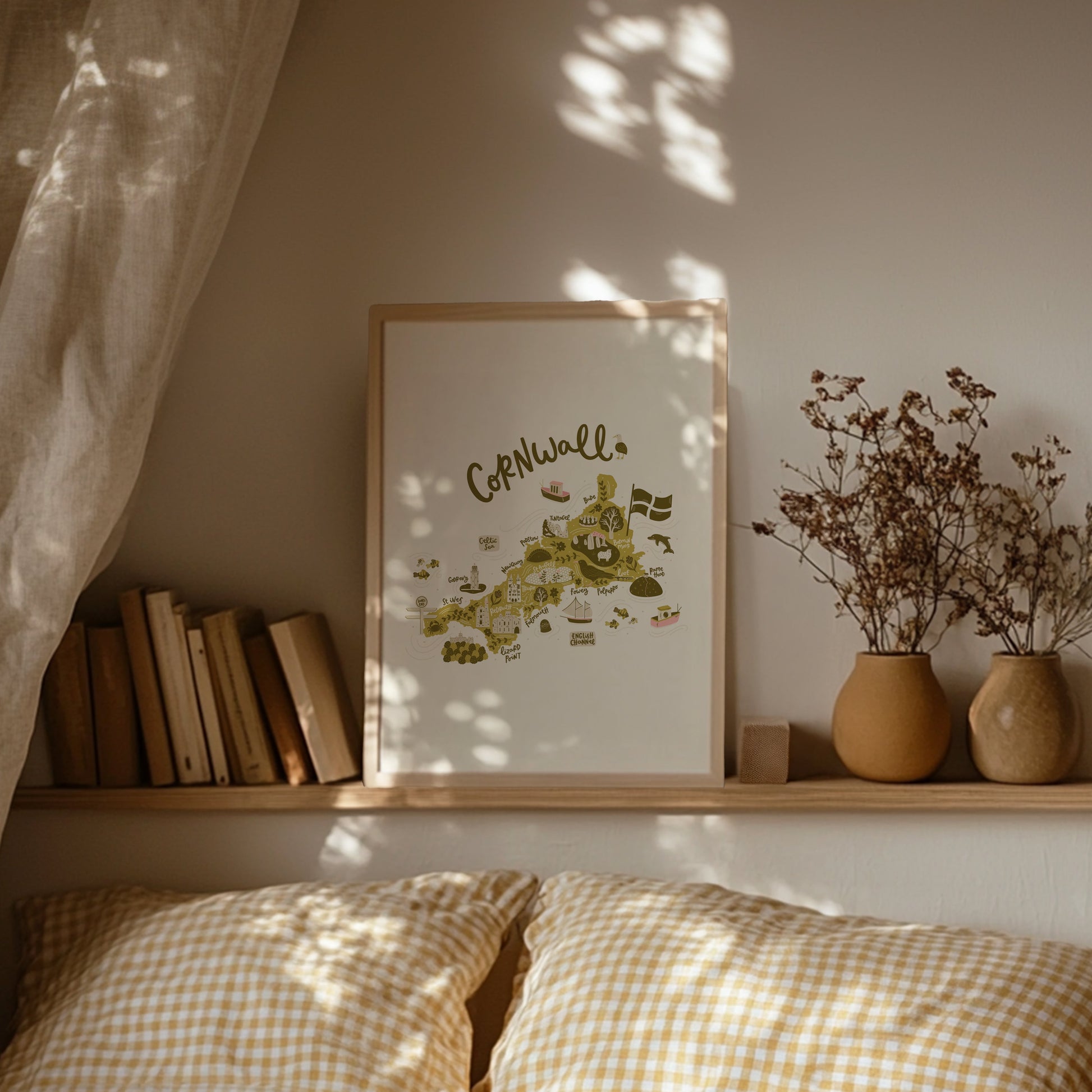 Lifestyle shot of illustrated Cornwall map print. Framed print on a shelf above a bed with gingham bedding.